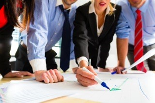 Business people standing around table, one writing