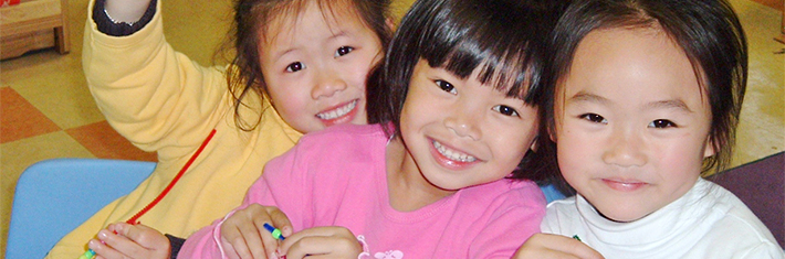 Photograph of three elementary school children cuddling together, looking straight at the camera and smiling