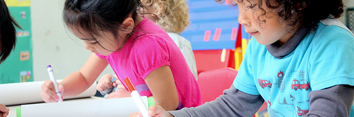 Photograph of two elementary school-aged children, coloring with markers in a classroom setting.