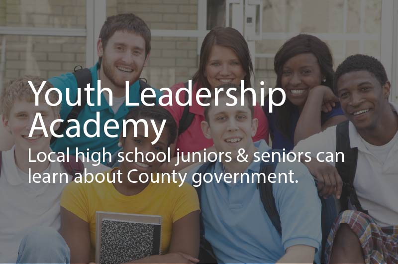 Photo showing a group of young adults smiling, with backpacks and looking happy to learn. Caption: Youth Leadership Academy. Local high school juniors & seniors can learn about County government.