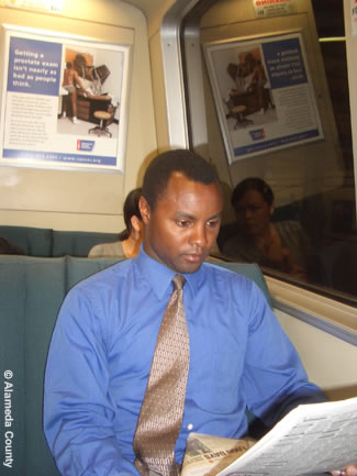 Photo shows County employee reading a newspaper while riding BART to work.